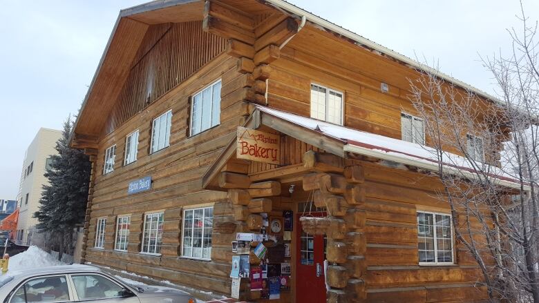 A two-story log building with a sign hanging out front reading, 'Alpine Bakery.'