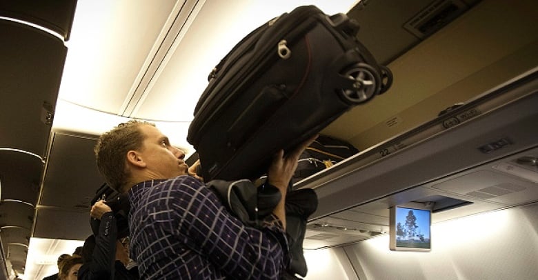 A man putting a carry-on suitcase in the overhead compartment on a plane. 