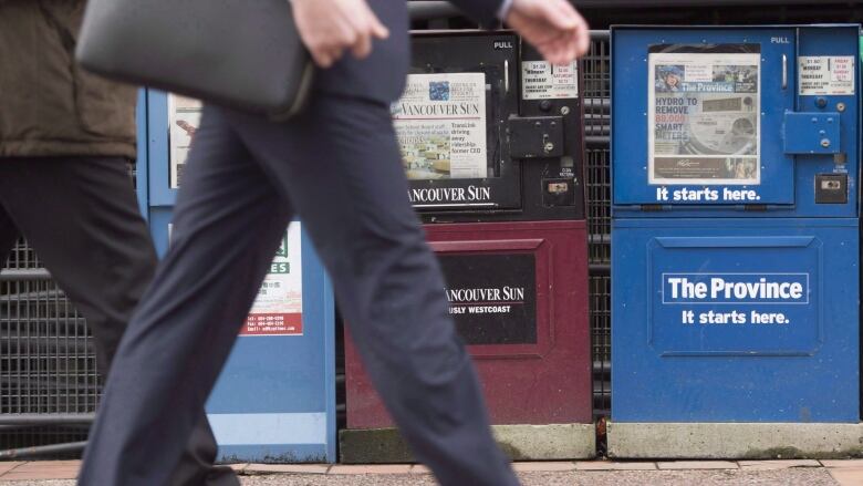 A man walks past newspaper boxes containing the Vancouver Sun and the Province in downtown Vancouver.