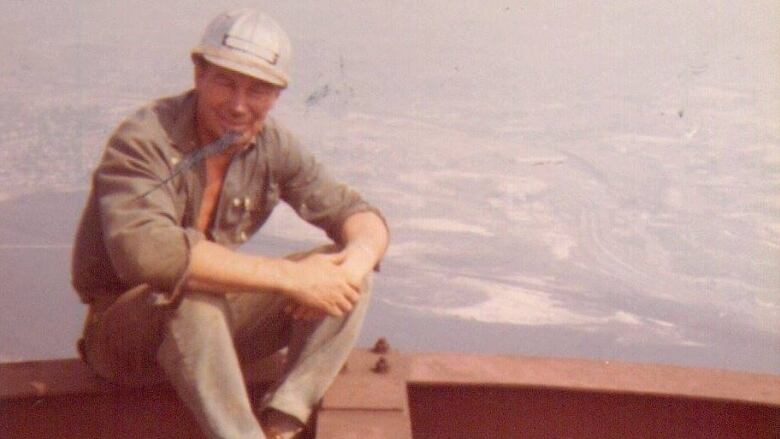 A man sits atop a construction site wearing a hardhat.