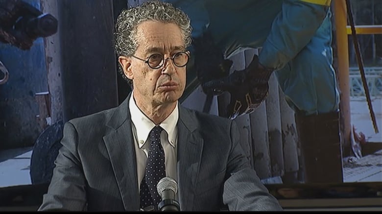 A man in a tie and jacket sits at a microphone.