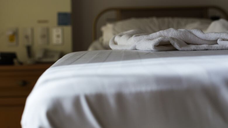 A bed can be seen with white sheets and a white blanket on top.