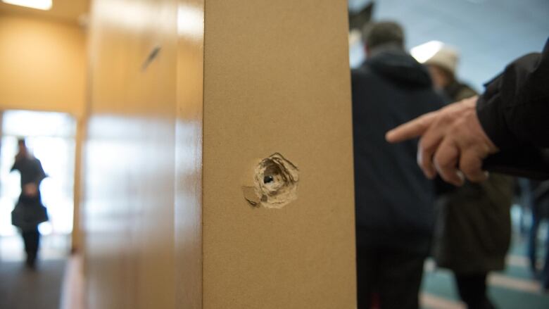 A person points to a bullet lodged in the column of a building. 