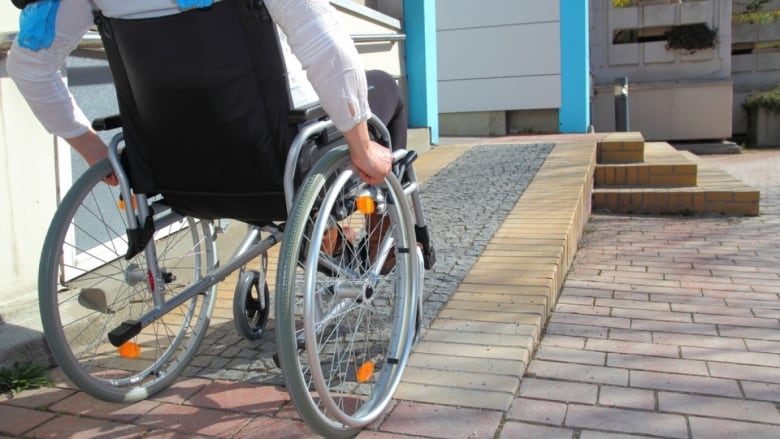 From behind, we see a person in a wheelchair going up a wheelchair ramp.