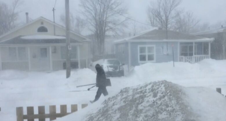 A person walking on a residential street through a blizzard. 