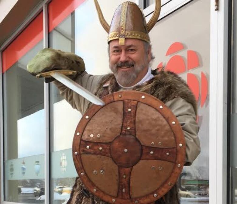 A man dressed in Viking attire poses with a fake sword. 