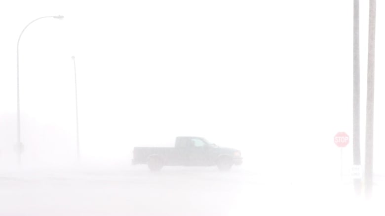 A truck is barely visible as it drives through heavy snow in blizzard.