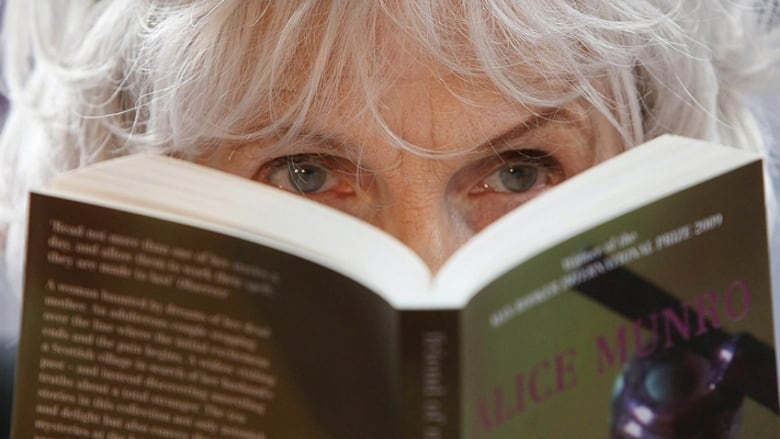 Author Alice Munro looks in the distance while reading one of her books. Her mouth and nose are hidden behind her book.