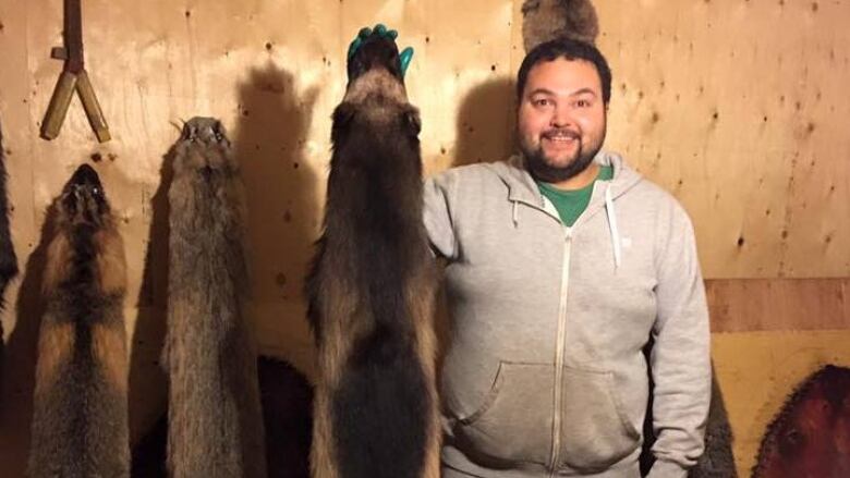 A man stands in a room holding up animal pelts