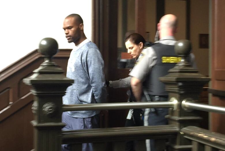 A man is escorted down the stairs of a courthouse by sheriffs.