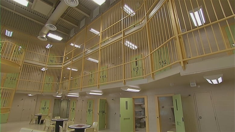 A common area of the Southeast Regional Correctional Centre in Shediac, New Brunswick is shown. There are several tables on a lower level, and a higher level showing a number of doors to cells.