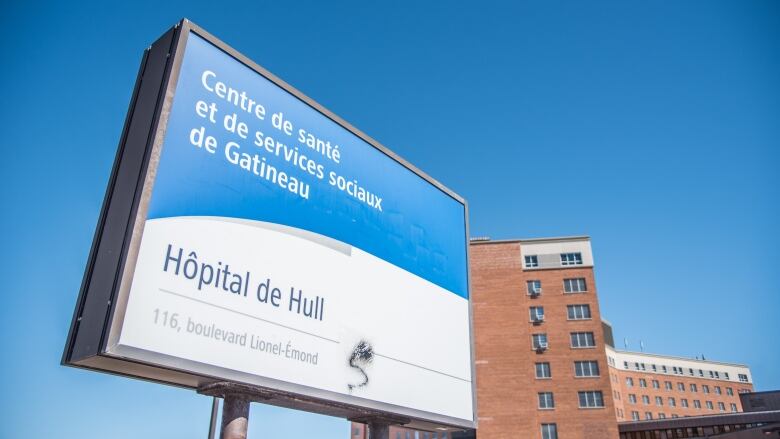 A blue and white hospital sign with a brick hospital building in the back.