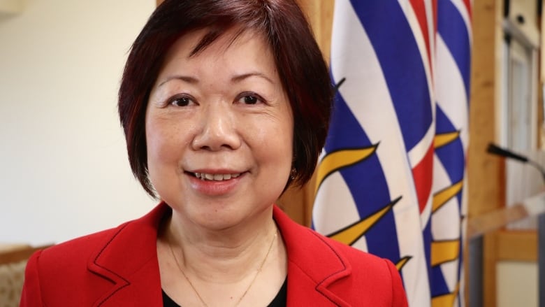 An Asian woman smiles in front of a B.C. flag.