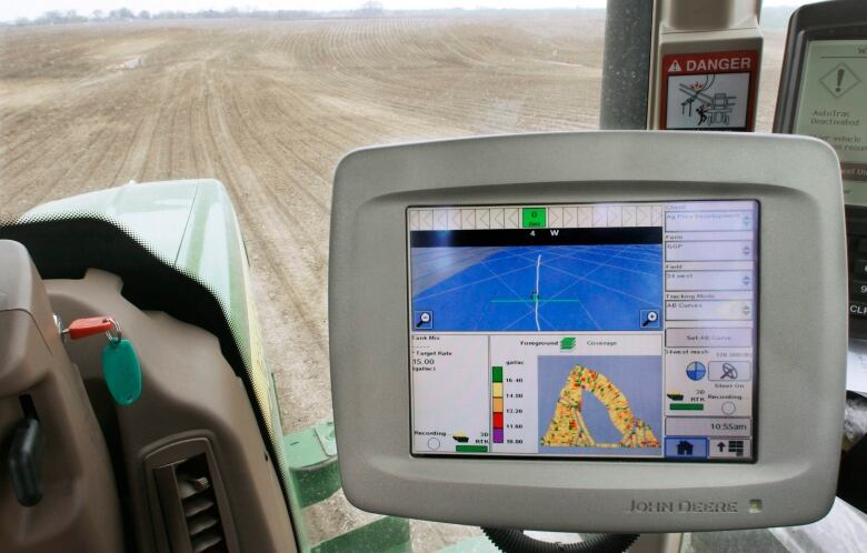 A computer monitor is seen inside a tractor cab with a farm field in the background.