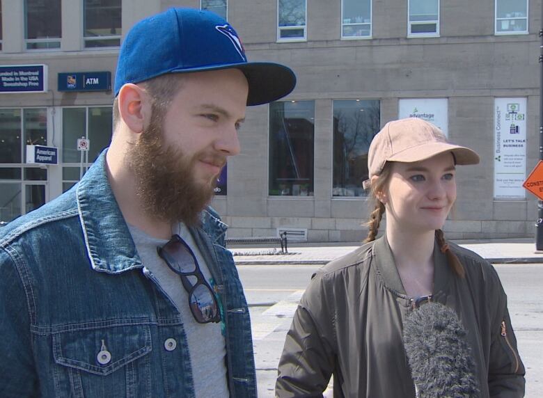 A man and a woman stand on a sidewalk.