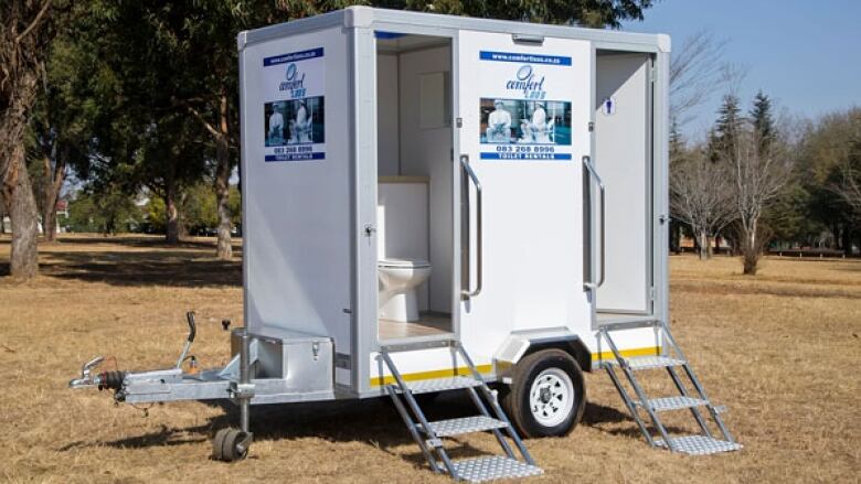 A white trailer on wheels with a staircase leading up into a small room with a toilet.