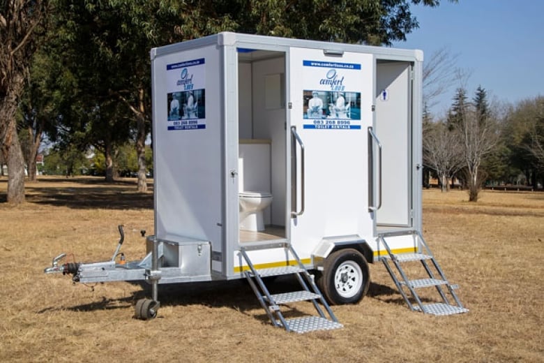 A white trailer on wheels with a staircase leading up into a small room with a toilet.