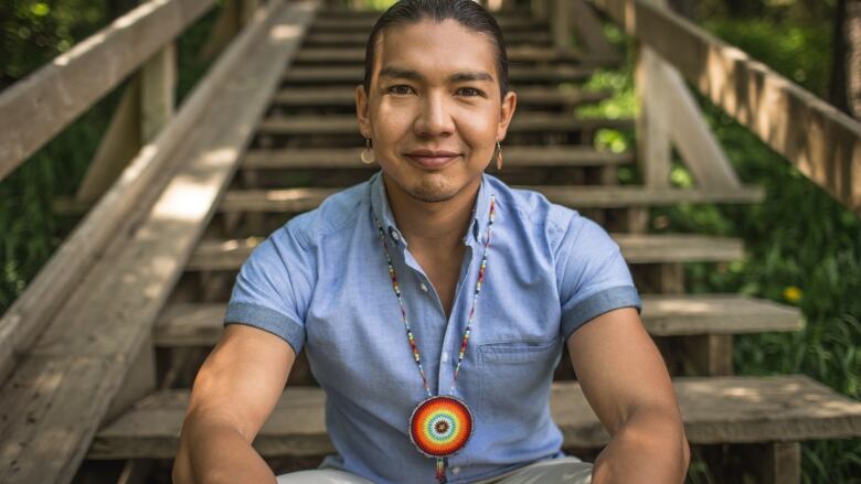 Dr. James Makokis sits on wooden stairs outside.