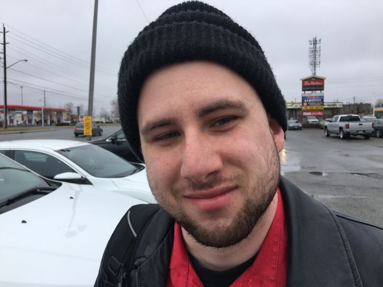 A young man standing in a parking lot, wearing a black toque.