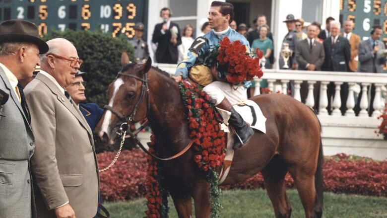 A jockey sits atop a horse, covered in roses.