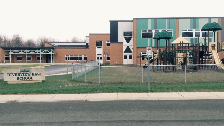 A school with a playground in front on the right and a sign that says 