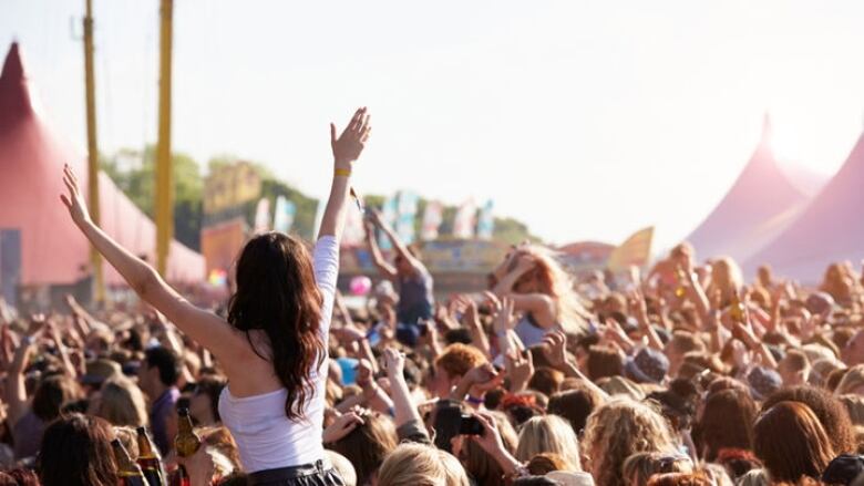 A woman puts her hands in the air in a crowd at a music concert.