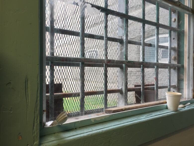 Dirty plastic spoons and a styrofoam cup sit on a dirty window ledge. Bars are on the window. 