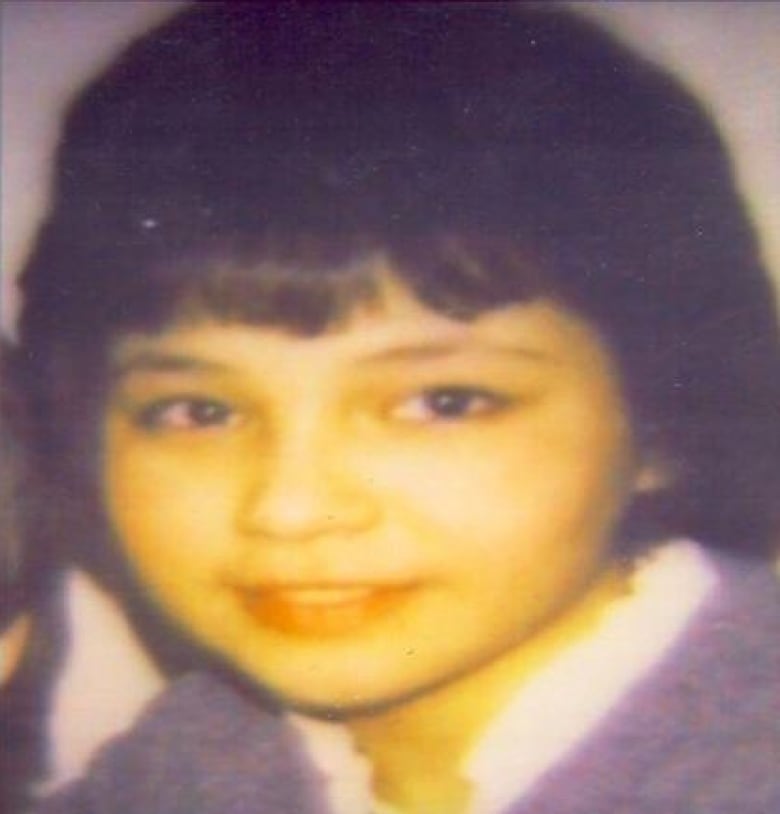 An old photograph of a girl with black hair wearing a blue jacket over a white shirt