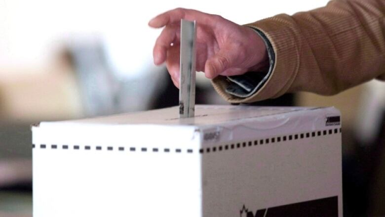 A hand is seen placing a ballot into a ballot box.