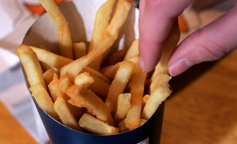 A close-up of a person reaching out to grab a french fry from a fast food container.