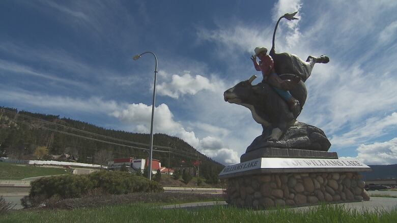 A city sign has a statue of a cowboy riding a cow.