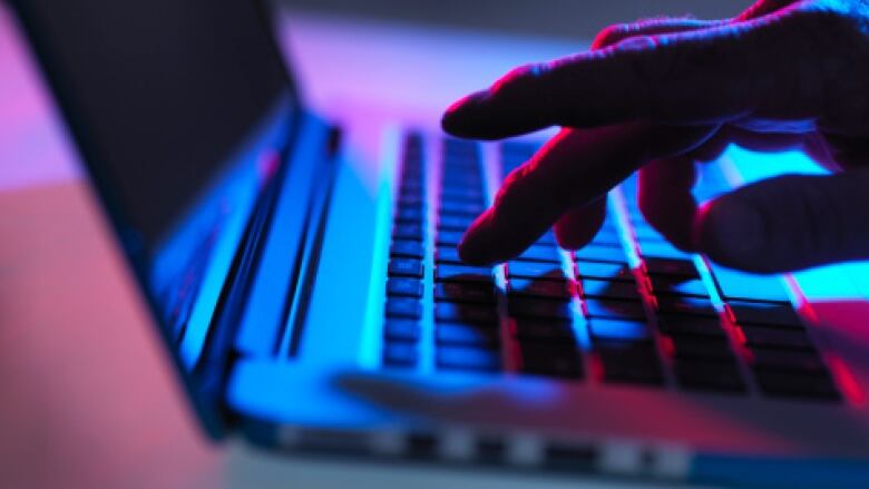 A hand types on a computer keyboard in a dark room.