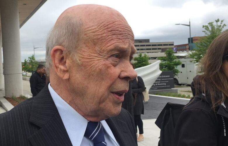 A side view of a balding man who is talking to reporters.