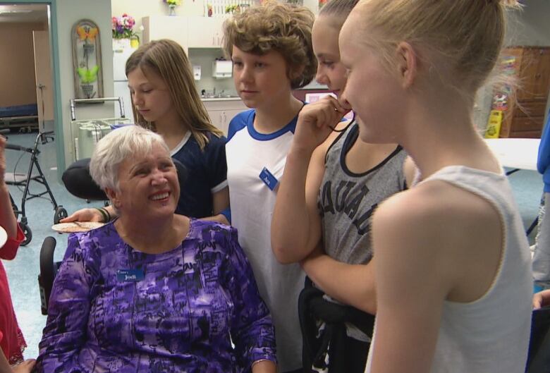 Jodi Grant sits in a wheelchair surrounded by happy Grade 6 students.