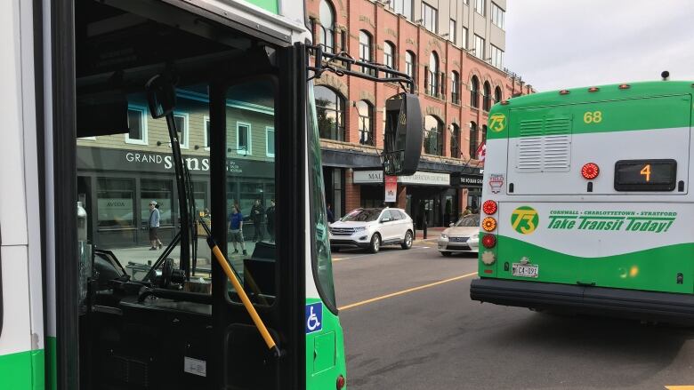 Two green and white coloured buses are shown parked along a street