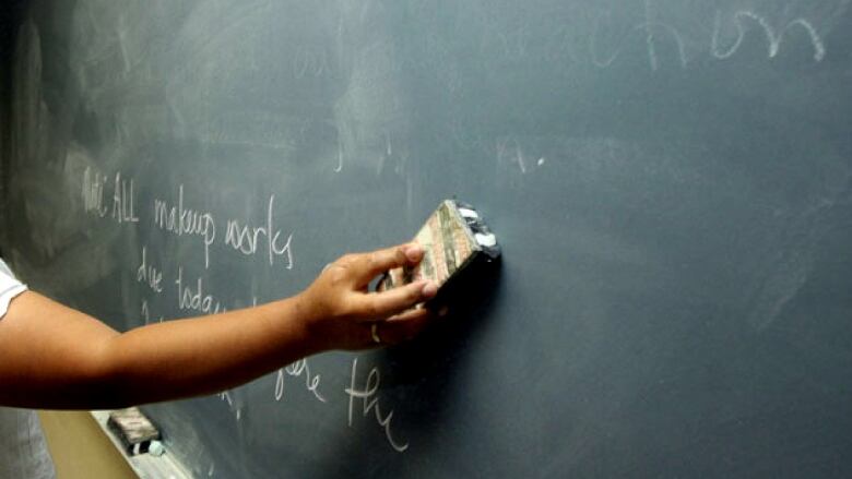 Close up of a teacher's arm using an eraser on a blackboard