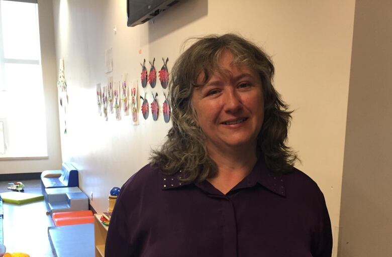 A woman stands in front of a playroom. Ladybugs on the wall are behind her head. 