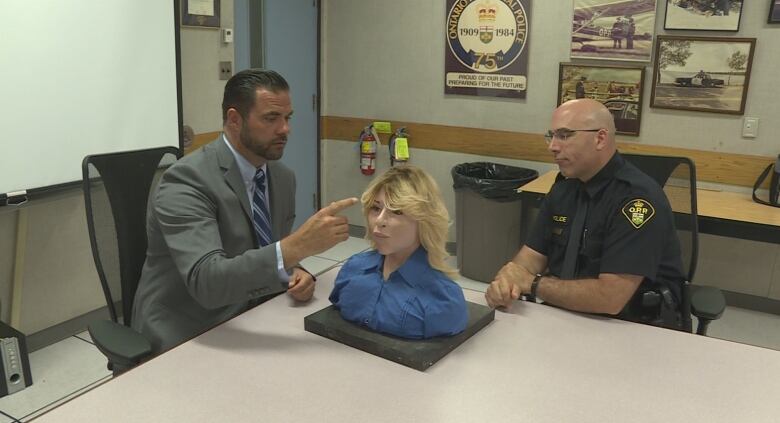 Two officers sit at a table with a clay bust reconstruction.