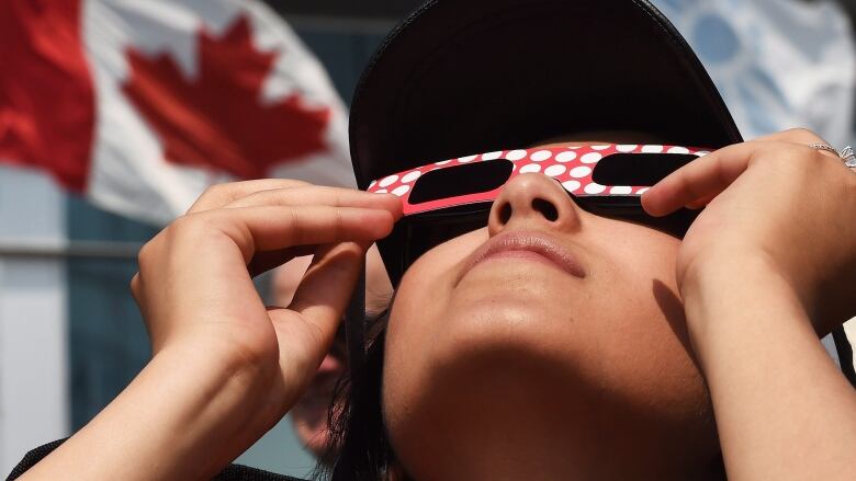 woman holding cardboard solar glasses looks at the sun