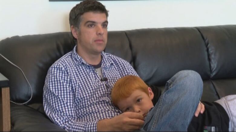 A man sits on a couch with a young boy.