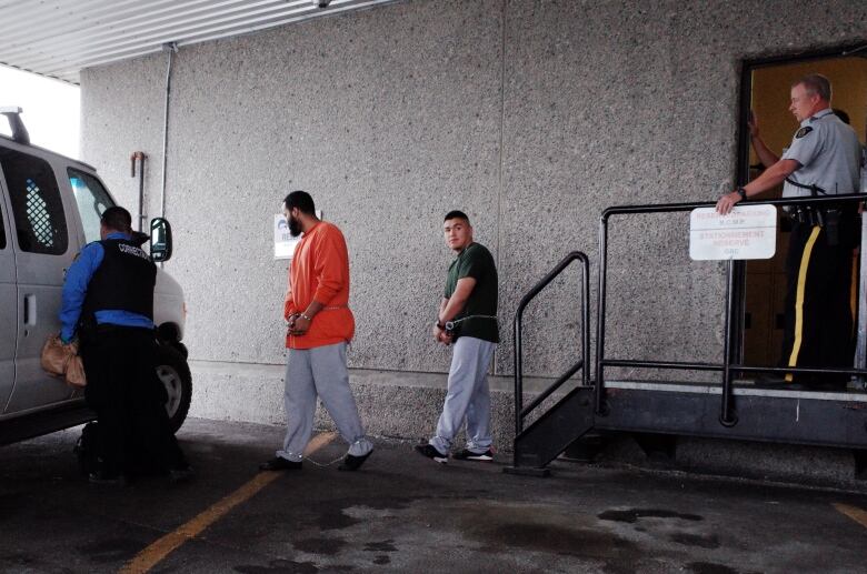 A man walks out of a courthouse in handcuffs with three other people around him 