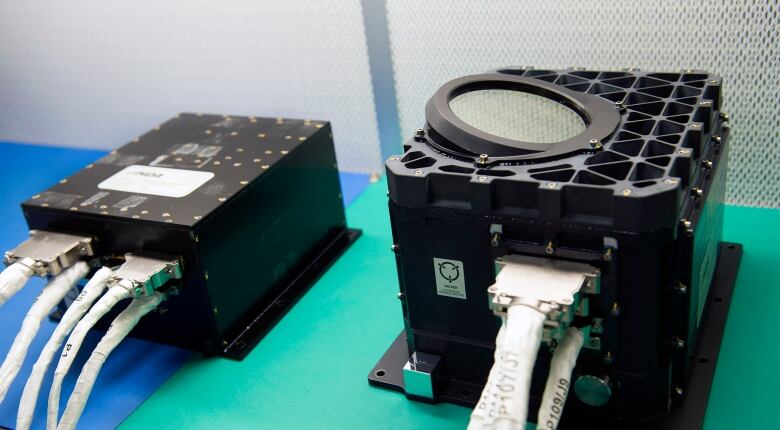 Two black boxes sit on a green table. On the left is an electronics box, and on the right is the two lasers that fired roughly three billion times to map out the asteroid Bennu.