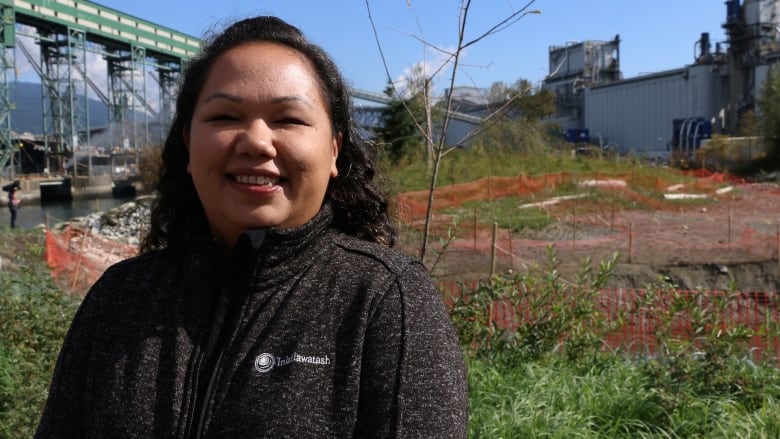 A portrait of an Indigenous woman smiling, with port infrastructure in the background.