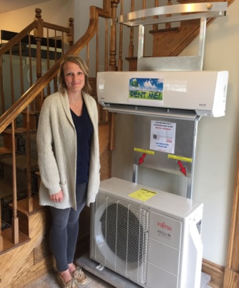 A woman stands beside the indoor component (top) and the outdoor component (bottom) of a ductless air-source heat pump.