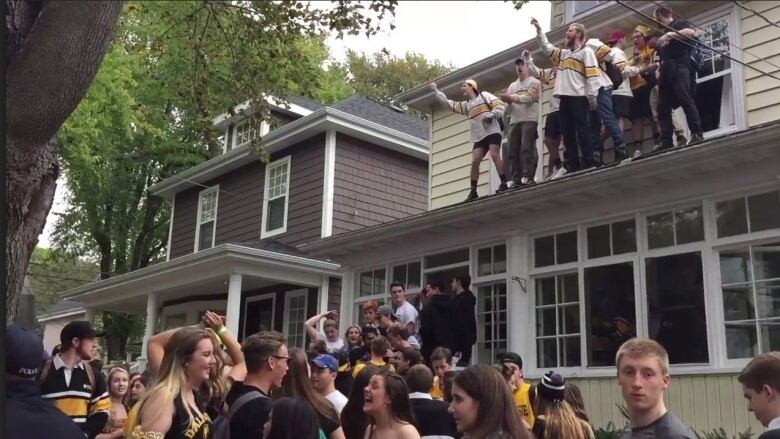 A screengrab of a video of a street party shows many students wearing black, yellow and gold attire, as well as people partying on a roof.