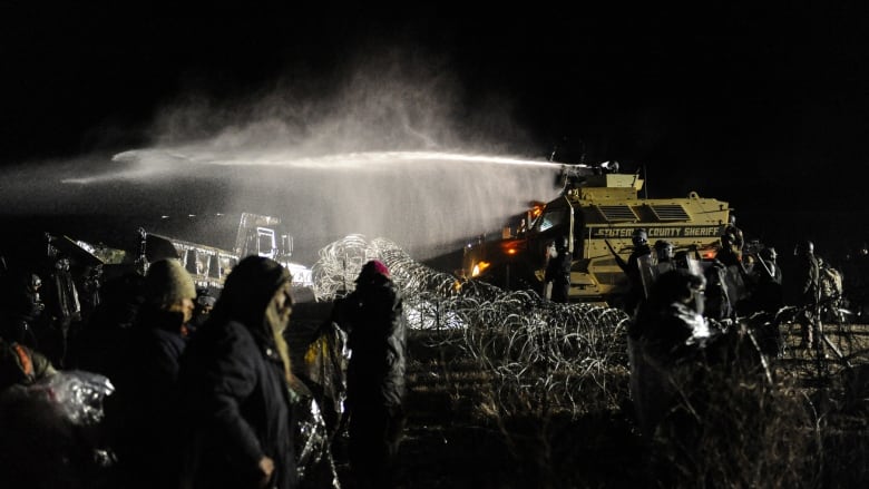 A water cannon sprays from an armoured vehicle in the darkness of night.