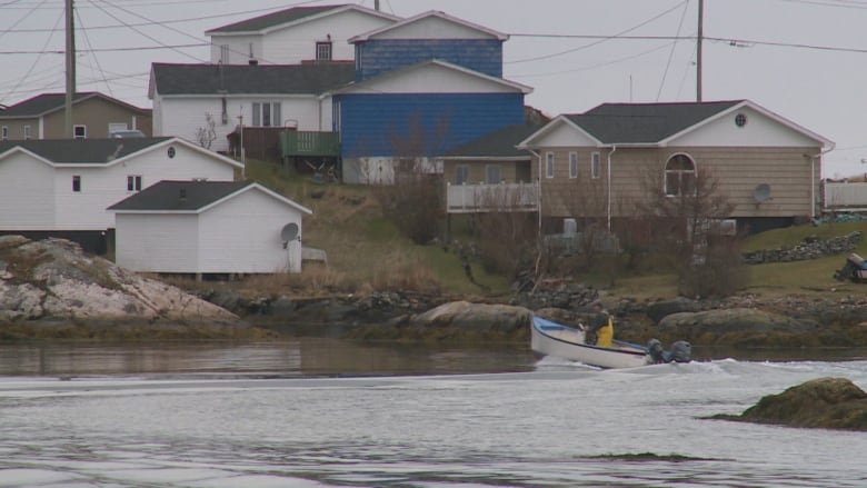 View from ocean looking at bunch of small houses along the shore, with a boat in the water.