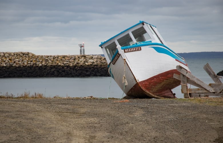 A small boat is shown tilting on it side on the ground.