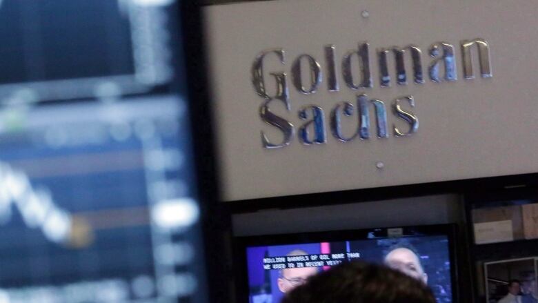 A screen at a trading post on the floor of the New York Stock Exchange is juxtaposed with the Goldman Sachs booth. 