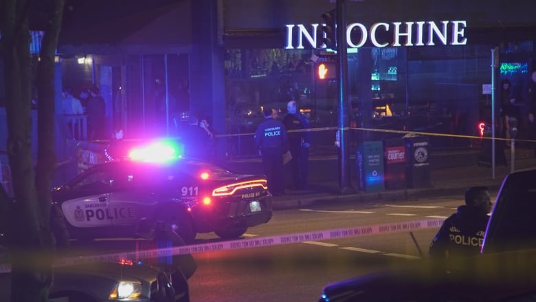 A police car is parked with lights flashing outside a restaurant cordoned off by tape.